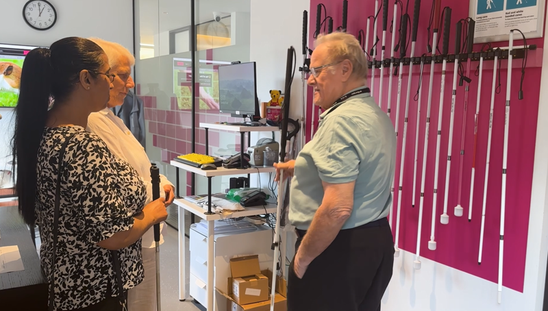 Amrit standing and speaking with an older man, in front of a wall of canes.