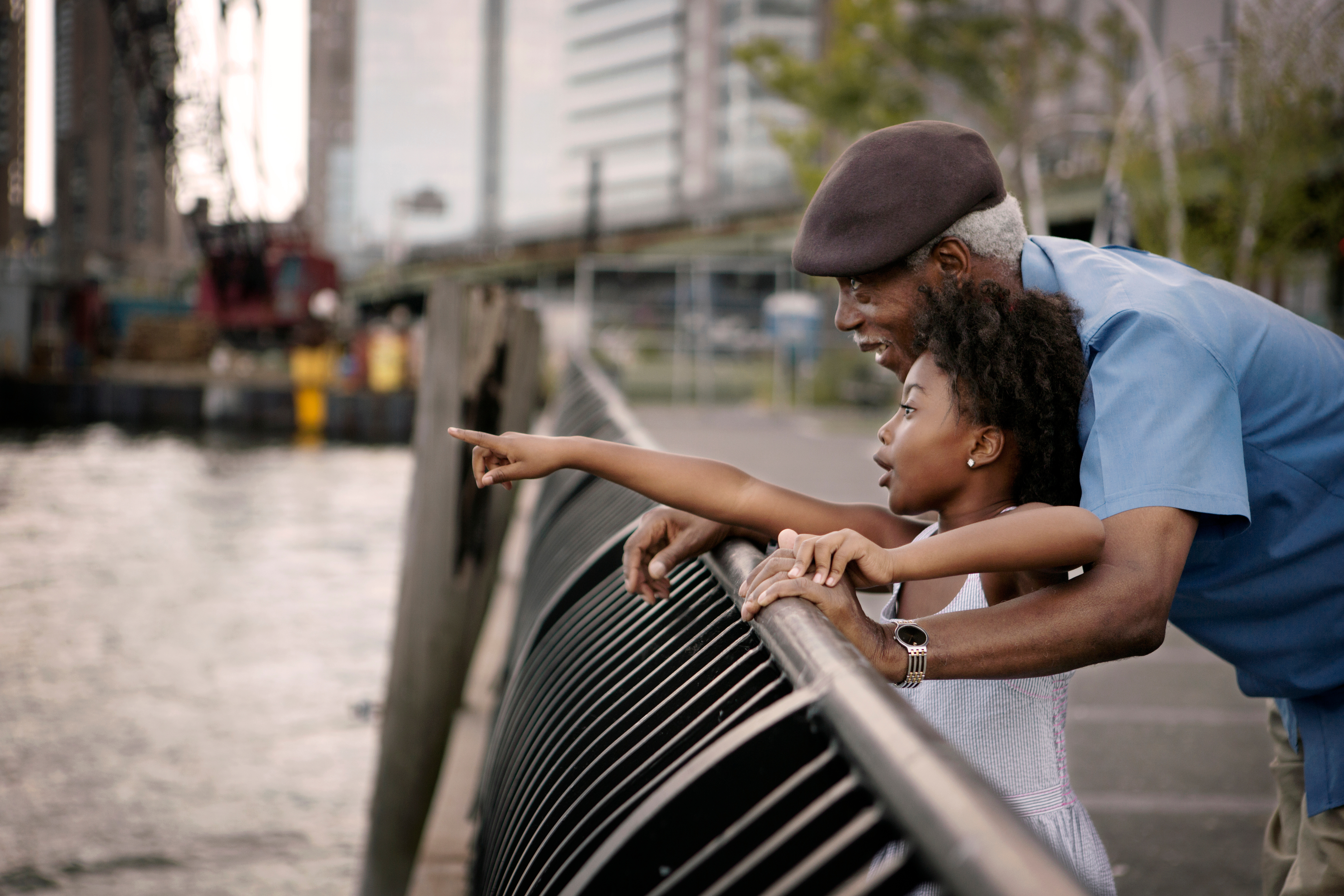 Man with granddaughter stood on a bridge pointing and smiling.