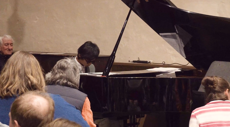 Chapman sitting at a piano and playing during a performance, with an audience watching him