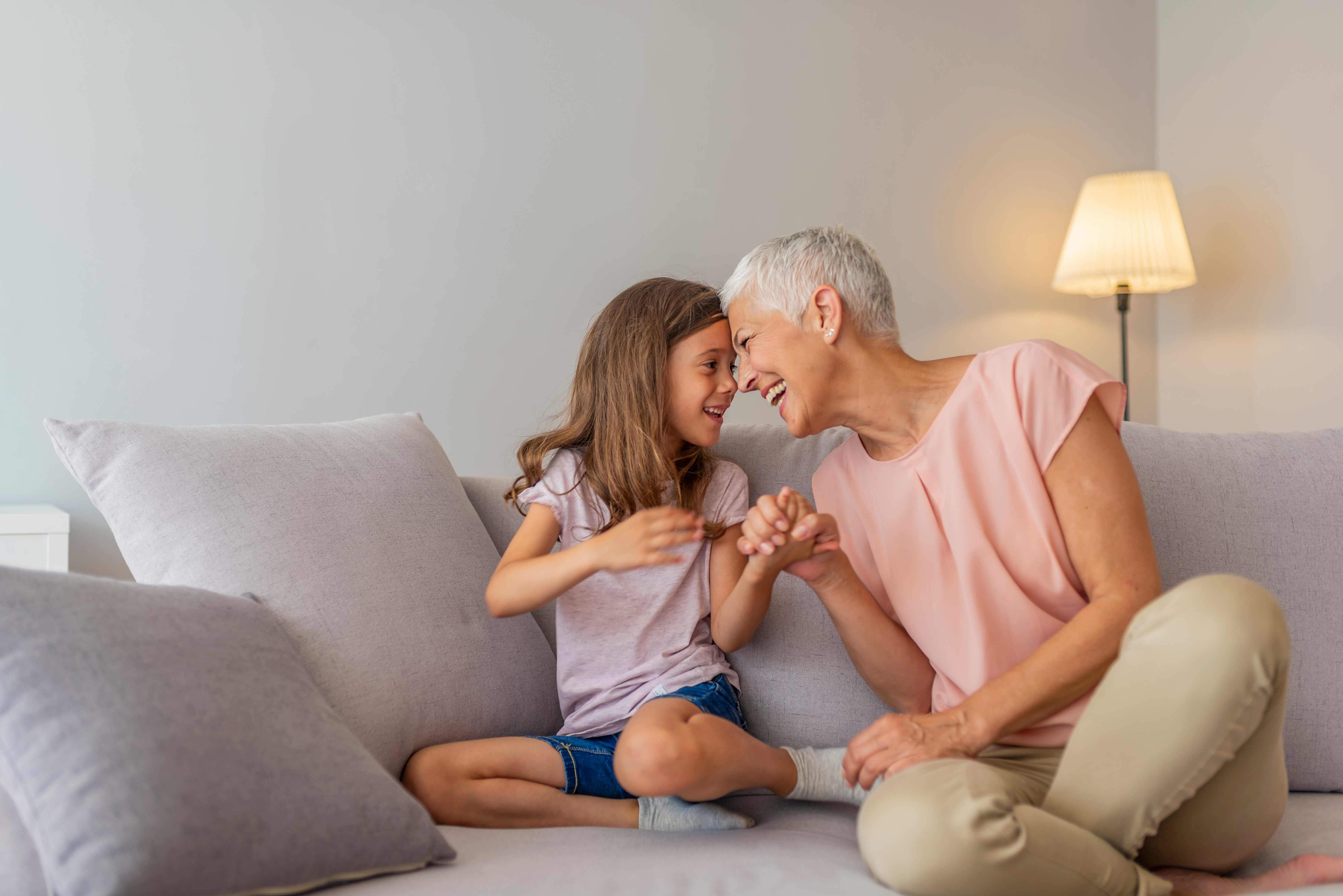 Photo of a Grandmother and Granddaugher sat on sofa smiling and holding hands.