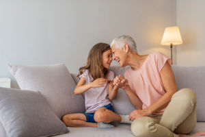 Photo of a Grandmother and Granddaugher sat on sofa smiling and holding hands.